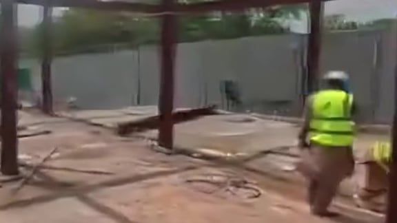 A site camera view of a steel-frame structure with a worker in a hi-vis vest walking across the slab