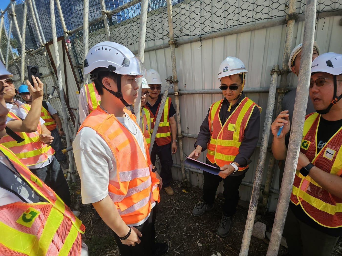 A site briefing with government and contractor staff, held beside site hoarding and scaffolding